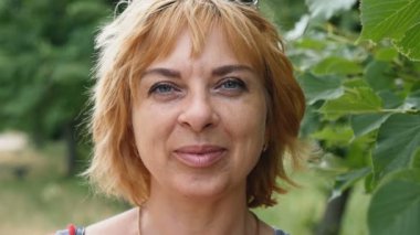 Ağır çekimde yaz yeşil bir parkta mutlu sarışın genç kadın gülümsüyor