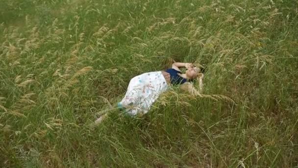 Молодая женщина в деревенском платье спит среди травы в солнечный день в сло-мо — стоковое видео