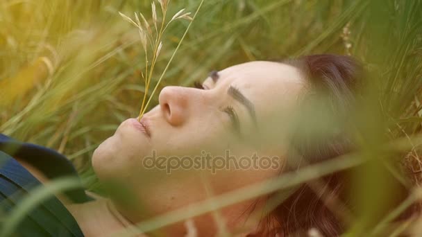 Menina romântica encontra-se em um gramado verde em um dia ensolarado no verão em câmera lenta — Vídeo de Stock
