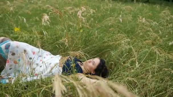 Jonge brunette meisje ligt op een groene gras, geniet van haar leven in de zomer in slo-mo — Stockvideo