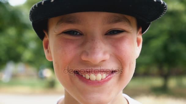 Egy boldog boy egy sapka mosolyog, állva, egy festői parkban slo-mo — Stock videók