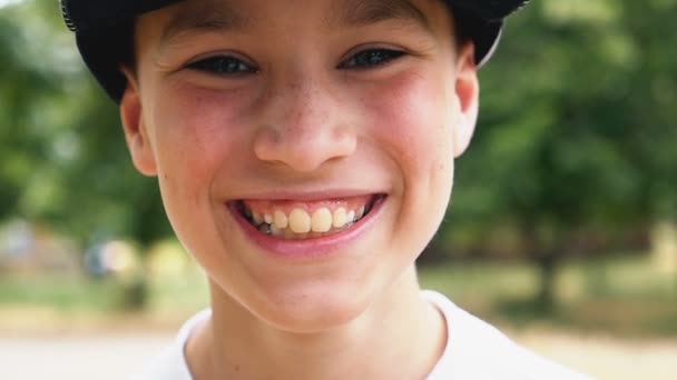 Веселый мальчик в кепке улыбается, стоя в живописном парке в сло-мо — стоковое видео