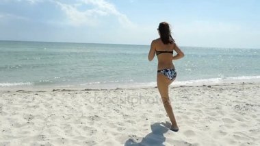 Bikinili güzel kız deniz sulara kumlu bir plaj üzerinde güneşli günü çalışır