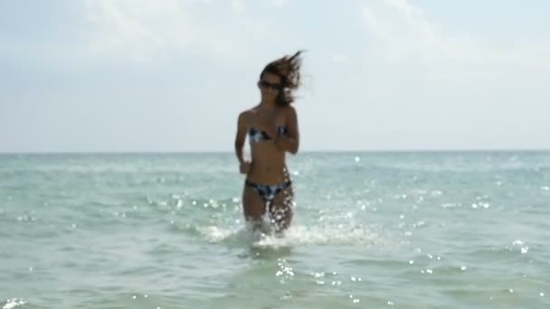 Стильная и стройная девушка в солнцезащитных очках бежит от моря к пляжу в slo-mo — стоковое видео