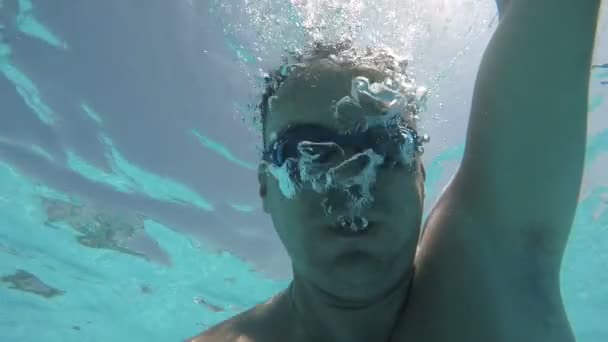 A un joven le disparan bajo el agua. Se siente feliz y hace grandes burbujas en un resort — Vídeo de stock