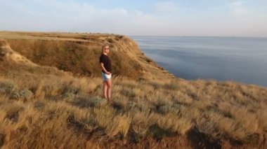 Günbatımında bir deniz cliff üzerinde duran cesur bir kadın hava 360 derece çekim