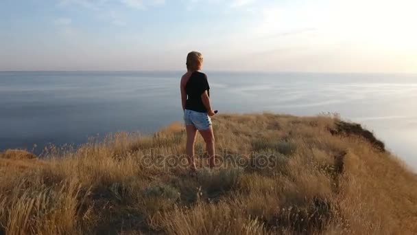 Aerial 360 degree shot of a stylish woman in sunglasses on a high seacoast hill — Stock Video