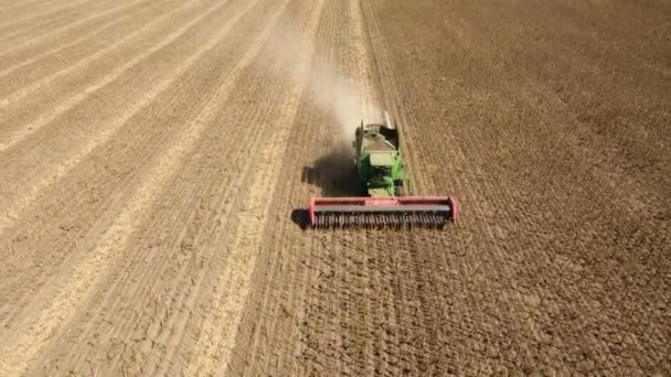 High flying drone winging before a green combine harvester gathering sunflower. — Stock Video