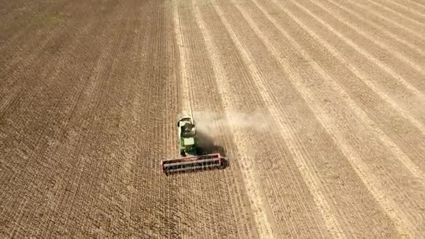 Een laag vliegende drone vliegt vooruit een combine harvester harken zonnebloem. — Stockvideo