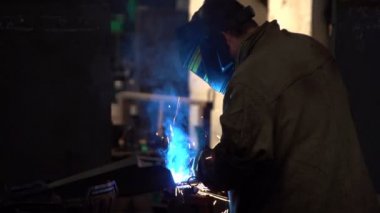 Parlak mavi ışık üreten bir kaynak makinası, üniformalı bir işçi kullanır