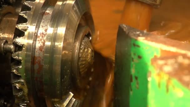 Öl ergießt sich auf einem sich drehenden Zahnrad mit einer Schneidvorrichtung in der Nähe in einer Werkstatt — Stockvideo
