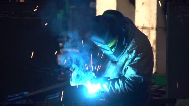 Un trabajador con una máscara de protección suelda una superficie metálica en un taller de una planta — Vídeos de Stock