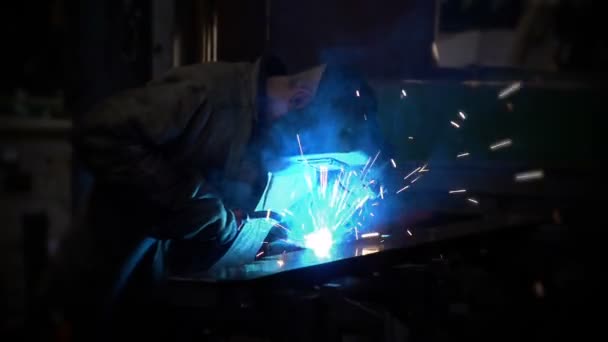Un trabajador en uniforme utiliza una máquina de soldadura, produciendo luz azul brillante — Vídeos de Stock