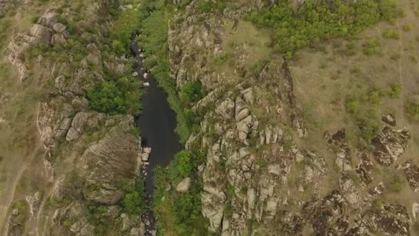   Une vue à couper le souffle d'une mince rivière noire se déplaçant dans un ravin entre d'anciennes roches brunes couvertes de nombreuses fentes en Ukraine en été ..