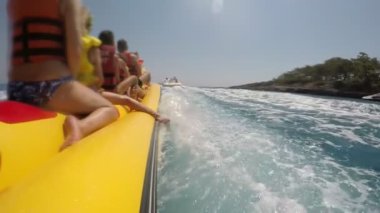 Mutlu turist Türkiye'de bir motoboat güneşli bir yavaş hareket sonra hareket büyük sarı muz sürme bir arka görünüm.