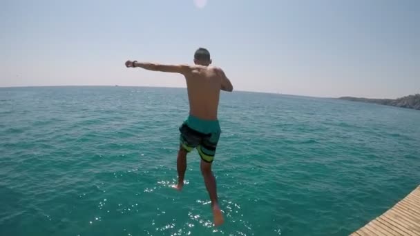 ターコイズ ブルーの海でジャンプする若い男の刺激的な表示の水フィート最初スローモーションで スポーツと幸せだね — ストック動画
