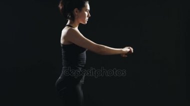 Bir at kuyruğu ile ince kadın bir yoga mat siyah bir stüdyoda mekik mekik siyah singlet ve pantolon giymiş yapan bir fitness eğitmeni ilham verici bir görünümünü yapar. Siyah bir spor salonunda enerjik yapıyor. 