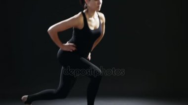 Bir at kuyruğu ile sportif kadın lunges bir yoga mat siyah Studio siyah bir sportif takım elbise giymiş lunges geri bir fitness eğitmen eğitici bir görünümünü geri. Siyah bir spor salonunda professionaly yapıyor. 