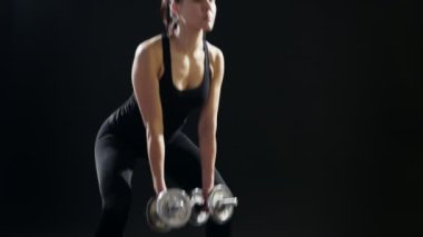 Fitness Eğitmeni ileri dumbbells sportif bir spor salonunda metalik dumbbells ile öne eğiliyor, ayağa kalkar, ileri spor salonunda kendini eğitimi sırasında görünüyor bir güçlü ve ince bir kadın inanılmaz bir görünümünü almak için eğilir.