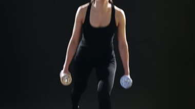 Genç kadın tutarken dumbbells bir stüdyoda onun elinde siyah bir takım elbise içinde onun elinde siyah bir stüdyoda metalik dumbbells tutarken lunges ileri bir sportif kadın etkileyici bir manzara lunges ileri 