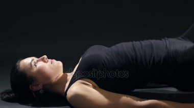 Sportif kadın arka tahta tutar ve vücudu kadar karanlık bir spor salonunda genç bir kadın vücudu üzerinde yatıyor ve onu geri vücudu karanlık bir spor salonunda tren yükseltir siyah elbiseli cesaret verici bir görünümünü yükseltir.