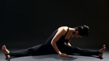 Sportif kadın yan bölme yapar ve bacaklarını bir spor salonu için. Bir tarafı siyah elbiseli genç bir kadını etkileyici bir manzara bölme ve virajlı kendini dışarı bir spor salonunda germe sırasında bacaklarına doğru.