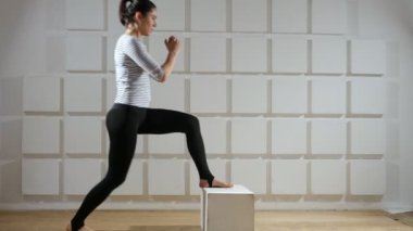 Sportif kadın ileriye doğru bir hamle yaparken bir küp yürüyerek genç bir ince kadın vücudu ise ileriye doğru bir hamle yapıyor ve bir spor salonunda küçük bir küp üzerinde onun ayak tutmak aşağı taşır öğretici bir görünümünü tutmak aşağı taşır.