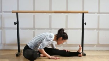 Sportif kadın oturur, bacaklarını uzanır ve bir spor salonunda, profesyonel fitness uygulamaları ve sportif bir spor salonunda oturuyor bir genç kadın eğitici bir görünümünü virajlı. O bacaklarını uzanır ve bacağını öne eğilir.