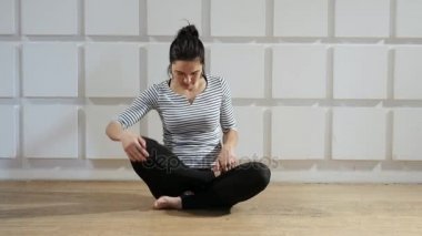 Genç kadın oturur ve bacaklarını bir lotus asana koyar. O heyecan verici bir görünüm o çizgili bir tshirt ve siyah pantolon bacaklarını bir lotus duruma soktuğunu bir kadın nefes başlar. O nefes ve gülümsüyor.