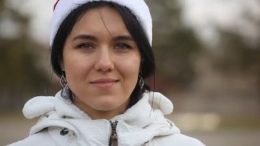 Esmer kadın beyaz bir anorak bir şehir sokak ve Kış A güzel esmer kadın gülümsüyor gülümsüyor üzerinde duruyor ve bir şehir sokak ve mutlu olmak gülümsüyor üzerinde duruyor. Kışın beyaz anorak ve beyaz şapka takıyor.