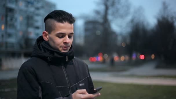 Jonge Man Staat Kijken Naar Zijn Mobiele Scherm Een Stad — Stockvideo