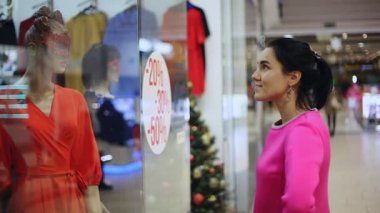 Mutlu kadın bir alışveriş merkezinde duruyor ve bir at kuyruğu yün elbise Noel hediyeleri tam bir alışveriş merkezi ile mutlu bir esmer kadın heyecan verici bir görünümünü bir alışveriş penceresinde görünüyor. O seçer Xmas hediye