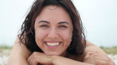Smiling woman lies on the Black Sea beach and laughs happily in summer in slo-mo                     A cheery view of a young brunette woman with wavy hair who lies on the sandy Black Sea beach, smiles and laughs, enjoying her life in slow motion.