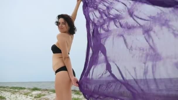 纤细的女人站在手上的披肩在黑海沿岸的一个快乐的年轻女子站在一个巨大的紫色披肩手在黑海岸边的风在缓慢的运动中飘扬 — 图库视频影像