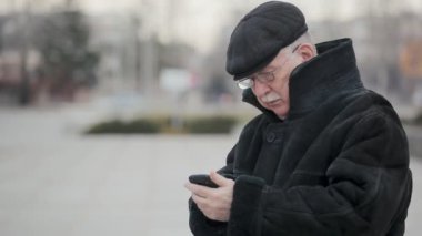 Bilge adam deri kürk paltolu bir şehir onun cep tarafından Kış A harika view diyen bir gri saçlı adam bir deri kürk ve deri kapağı, bir sokakta cep telefonunu tarafından kışın sokak çağırır.