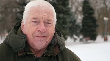 Neşeli gri başlı adam anlamına gelir ve slo-mo kışın gülümsüyor. Eski bir bilge adam iyimser bir closeup bir sanatsal sokak sokak slo-mo kışın üzerinde duran bir koyu yeşil anorak giymiş. Kendini iyi hissediyor