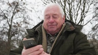 Üst düzey gri başlı adam standları ve slo-mo kışın mobile tarafından çağırır. Kim bir şehir sokakta duruyor ve kış slo-mo tarafından mobil aramalar koyu bir yeşil anorak özgün bir görünümü bir yaşlı bilge adamın giymiş.