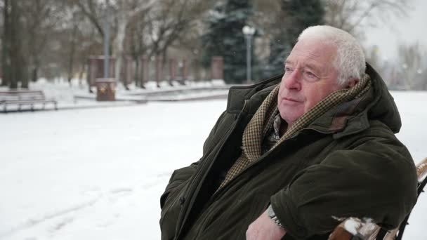 老灰头男人坐在那里 想着他在斯洛伐克的冬天的生活 Originalview 的老人穿着一个深绿色的皮猴谁坐在一条小巷的长凳上 想着他的生活在冬天在斯洛伐克莫 — 图库视频影像