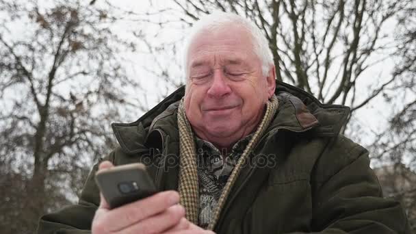 在斯洛伐克的冬季 资深的灰为首的男子站在移动电话 一个老智者的原始看法 穿着在一个深绿色的皮猴谁站在城市街道 并呼吁在冬季移动在斯洛伐克莫 — 图库视频影像