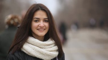 Mutlu kız uzun bağsız kıl ile çekici bir esmer kız kış A closeup bir sokakta romantik uzun bağsız kıl gülümsüyor. O bir sokakta harika beyaz kaşkollu ile kışın duruyor