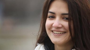 Samimi kız uzun bağsız kıl gülümsüyor açık-heartedly içtenlikle mutlu olmak gülmeyen bir güzel esmer kız kış A closeup içinde açık havada. O bir şehir kış aylarında sokak üzerinde yün şapkasız standları