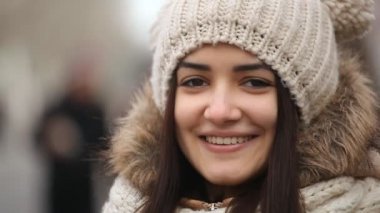 Mutlu kız gülümsüyor ve tribünde komik örgü şapkasına bir gülümseyen kız kış A neşeli portre bir sokakta bir anorak uzun gevşek saç ile topları ile ve kış sokakta komik topları ile örme şapka