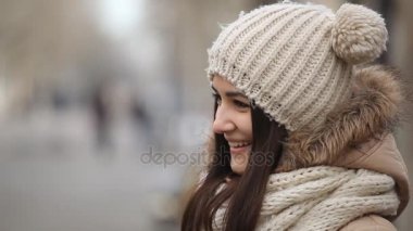 Samimi kız gülüyor ve neşeli örgü şapkasına bir sokak topları ile kışın gülünecek bir kızın inanılmaz bir profil bir anorak ve örme şapka uzun saçlı komik taşaklı bir ara sokakta kışın ayakta duruyor