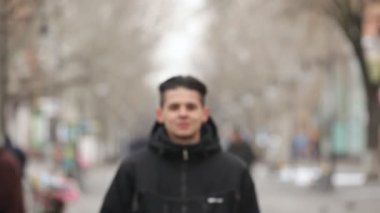 Şık bir genç adam gülümsüyor ve pitoresk bir sokak kışın bir masal Sokağı ile rahatlatıcı seyir boyunca yürüyüş bir kürk anorak genç bir erkekte iyimser bir bakış yürüyor insanlar kışın güneşli bir günde