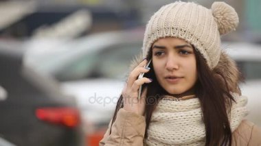 Onu tarafından beyaz yepyeni bir araba mobil arama neşeli genç bir kadın örme şapka bir kürk anorak toplar, harika bir manzarasını onun mobil bir otopark gülümseyen kız bir anorak ve örme şapka konuşuyor. 