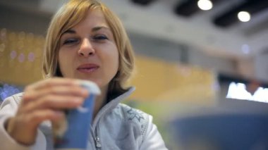 Mutlu sarışın kadın gülümsüyor ve içecekler gülümsüyor ve bir kafeteryada oturur ve sıcak kahve içiyor bir neşeli sarışın kadın iyimser bir bakış kışın sıcak kahve bir kafeteryada. Bir gri zipup kazak kız