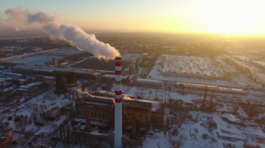 Beyaz ile çok yüksek bir sıcak gaz baca hava atış kışın günbatımında bir kuş bakışı büyük bir baca ve duman yavaş akışı ile kışın harika bir gün batımı, duman. Bir fabrika duruyor ve evler.