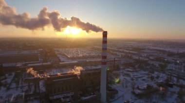 Gökyüzü hurdaya sıcak gaz hava atış ile beyaz duman kışın günbatımında bir kuş bakışı gök yüksek baca ve duman yavaş akı ile kışın harika bir gün batımı, kule. Bu bir bitki duruyor. ve evleri.