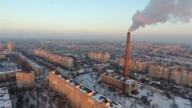 Hava yüksek doz yavaş yavaş kış gün batımında duman yetiştirme ile gaz baca kışın günbatımında bir özgün kuş bakışı bir yüksek sıcak gaz baca ve duman yavaş bir akış ile sıcak. Bu şehir evleri arasında duruyor.