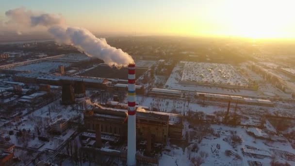 冬季日落时 一座高耸的热气烟囱的空中拍摄 在冬天的夕阳下 一只巨大的烟囱 一只小鸟的眼睛看着一条缓慢的烟雾 它站在工厂和房子附近 — 图库视频影像